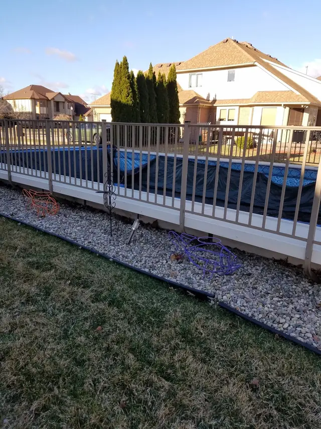 Wood-frame pool with a deck railing and stone border in a suburban back yard