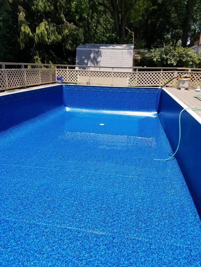 Empty rectangular pool with a fresh blue patterned liner behind a white lattice fence