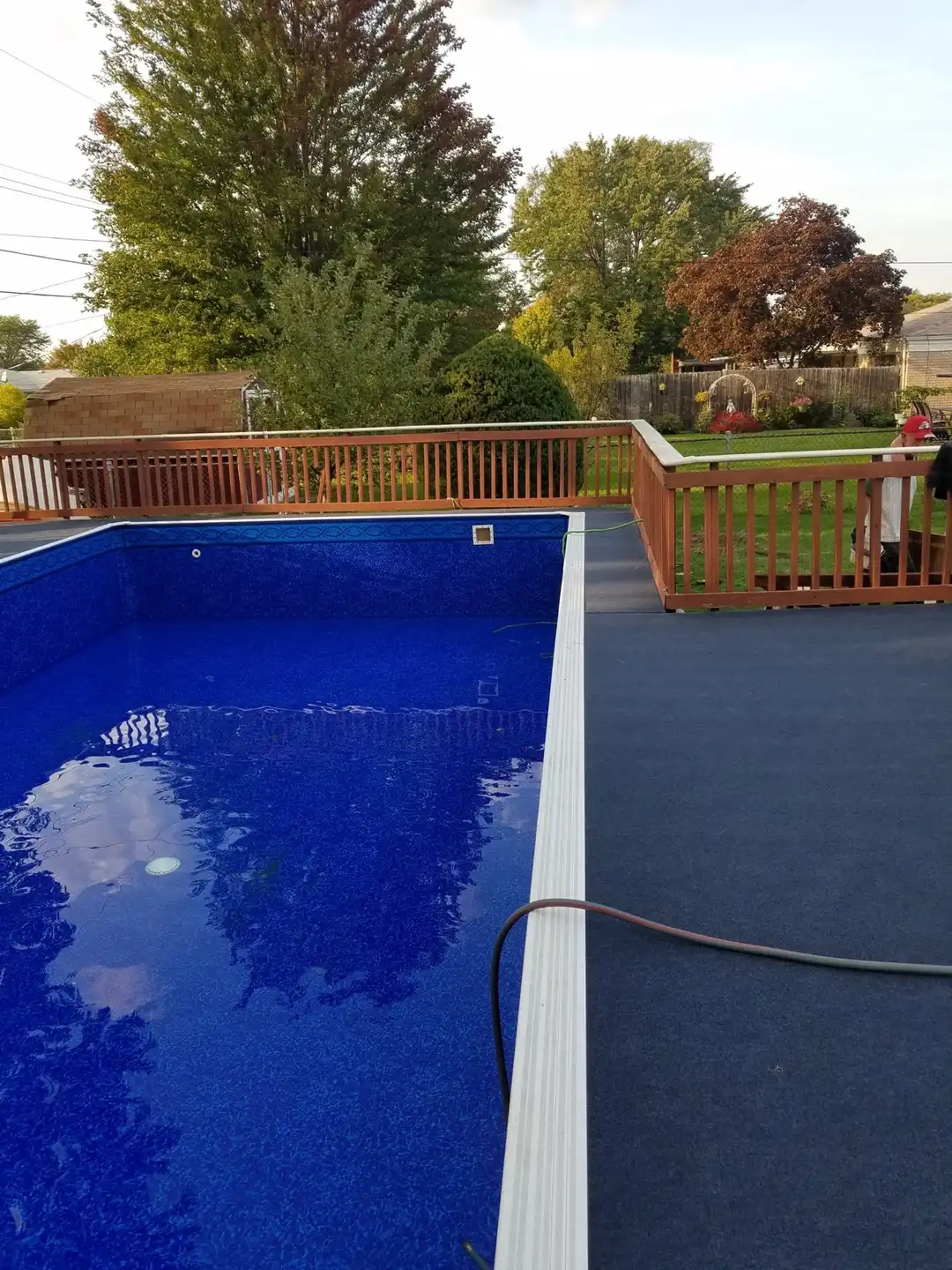 A rectangular pool with a new deep-blue liner, filled to the skimmer, beside a wood deck and railing